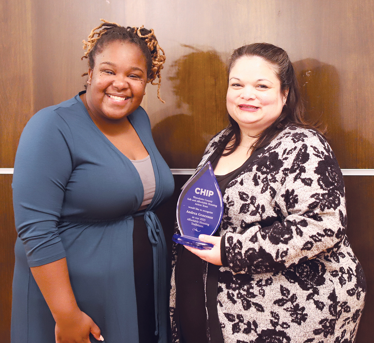 Two women stand next to each other and the woman on the left is holding an award