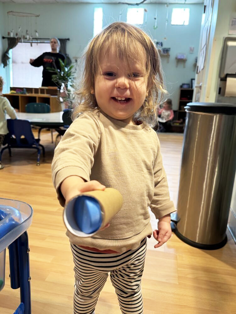 A toddler places a ball in a cardboard tube