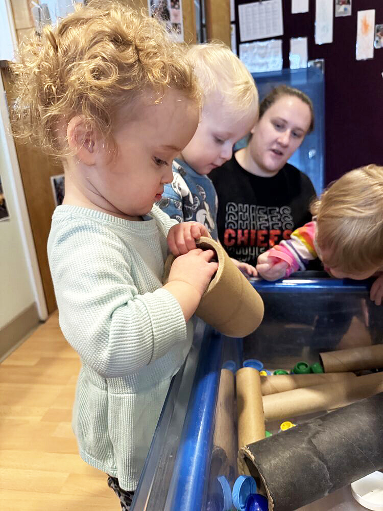 A toddler places a ball in a cardboard tube