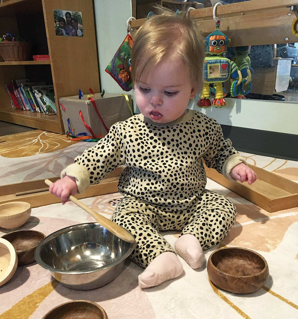 A toddler plays with a wooden spoon and various bowls