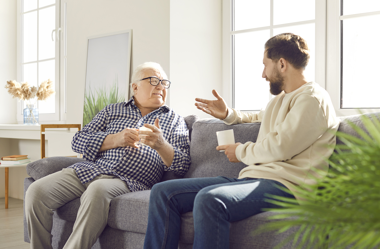 Two men, one elderly, speaking to each other on a couch