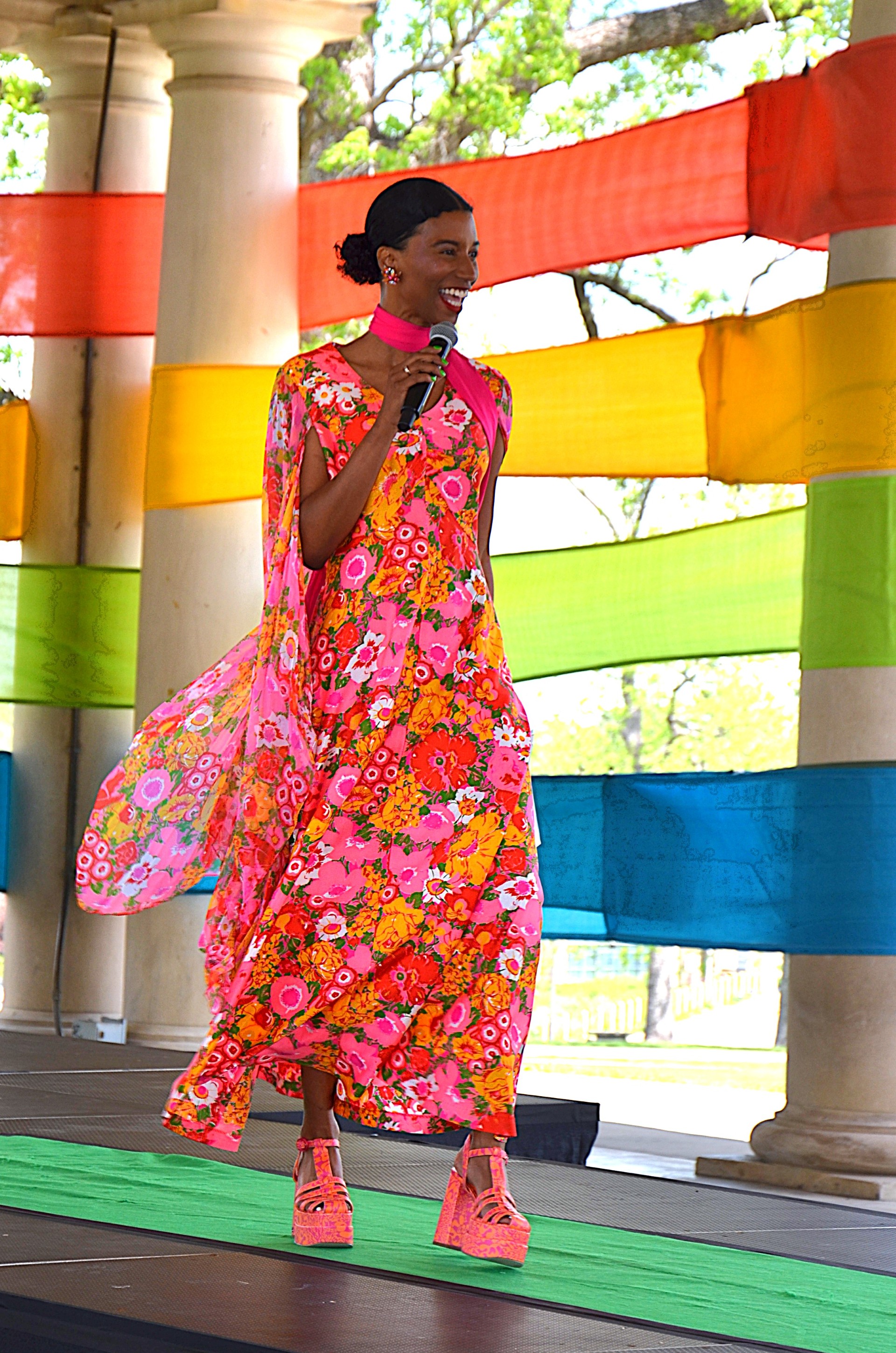 Emcee walks the green carpet runway dressed in pink flowery fashion gown