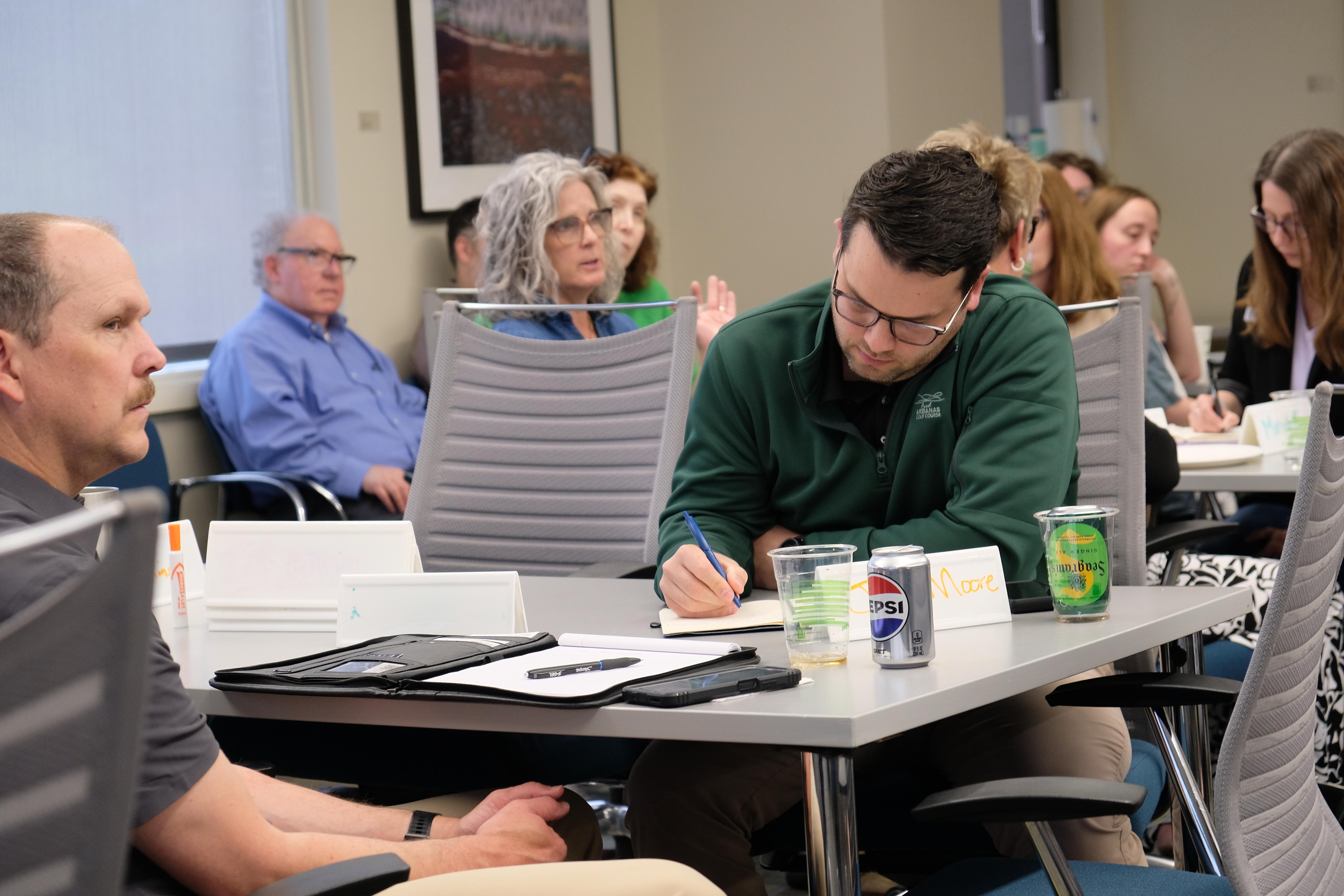 Man in green shirt at grey table taking notes