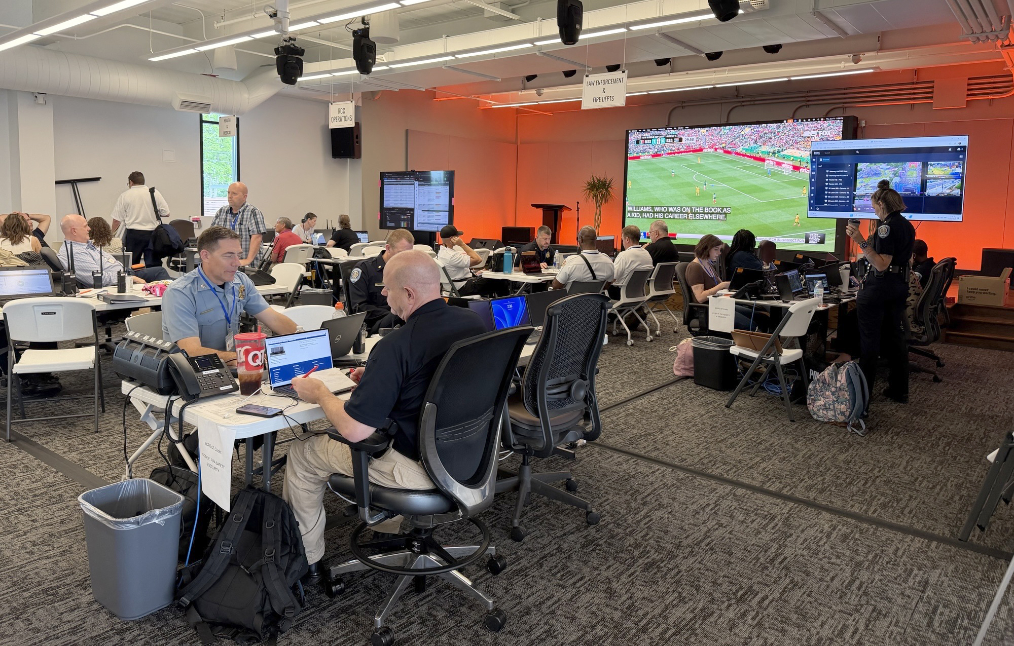 A room full of people sitting at tables with a soccer match on a screen