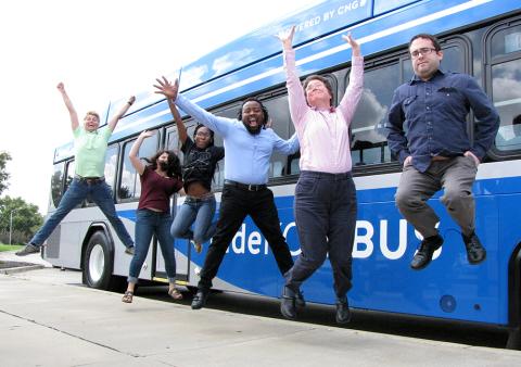 Six people jumping in the air while standing beside a bus