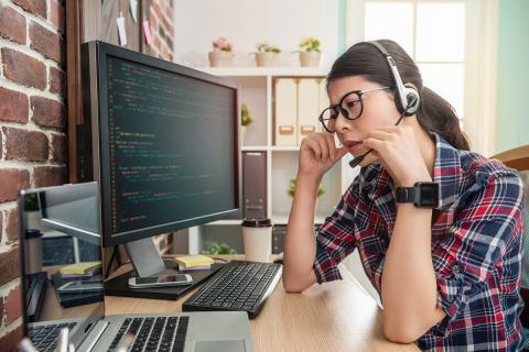 A person at a desk talking on a head set and looking frustrated