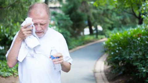An older man wipes sweat from his head and holds a bottle of water