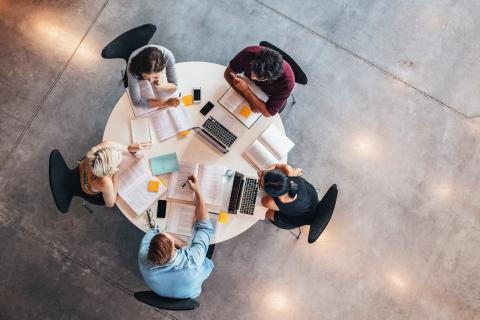 Overhead shot of a table with five university students doing academic work 