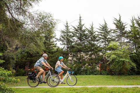 Two individuals ride bikes in the park