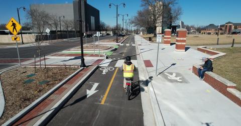 Rider in high visibility vest tests out new two-way separated bicycle lane offset from street with refuge islands and other pedestrian upgrades