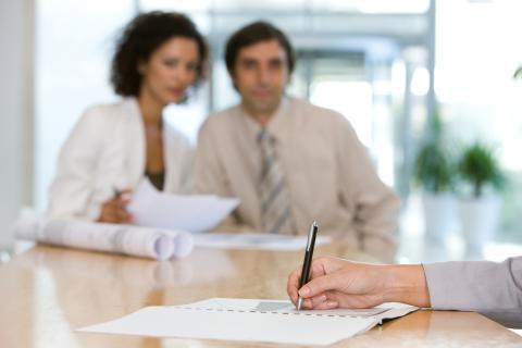 Person writing notes with a pen as two co-workers look at them 