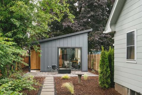 A detached image of a slanted ADU home behind the main home framed by trees