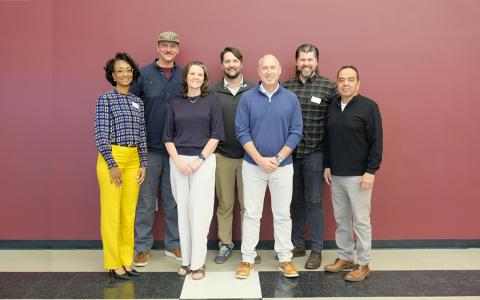Housing forum attendees stand in front of a burgandy wall.