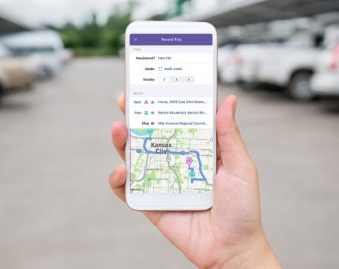 A person holding a smart phone with the WAY TO GO trip planner on the screen.