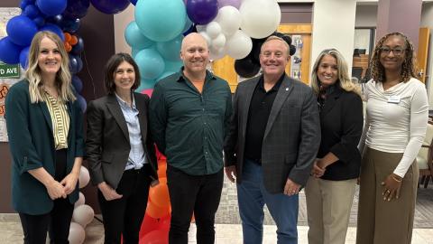 Panelists in a row, smiling, in front of balloons.