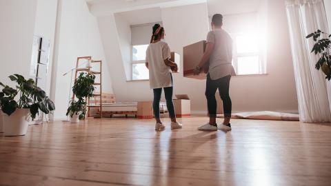 A couple holding moving boxes in a mostly empty apartment