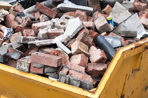 Yellow dump truck bed filled with broken masonry bricks and other assorted demolition waste