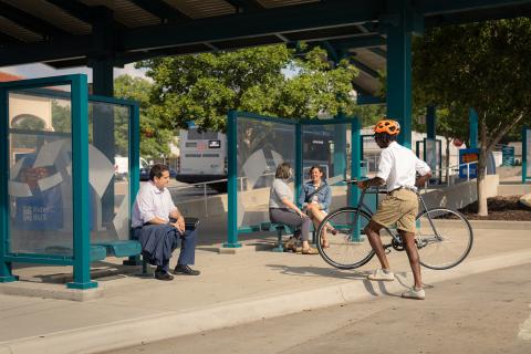 A person carrying a bike to a covered bus stop where other people wait