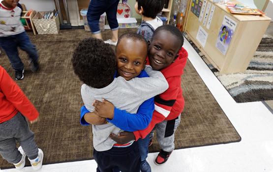 Young children smiling and hugging in a classroom