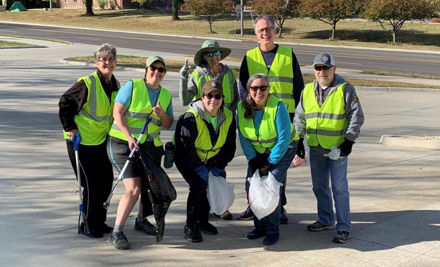 volunteers in neon yellow vests pose with bags and grabbers at public trail