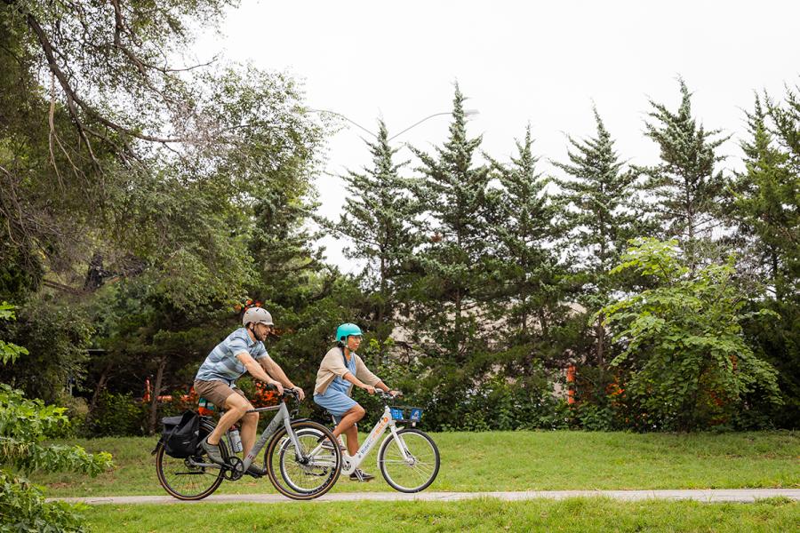 Two individuals ride bikes in the park