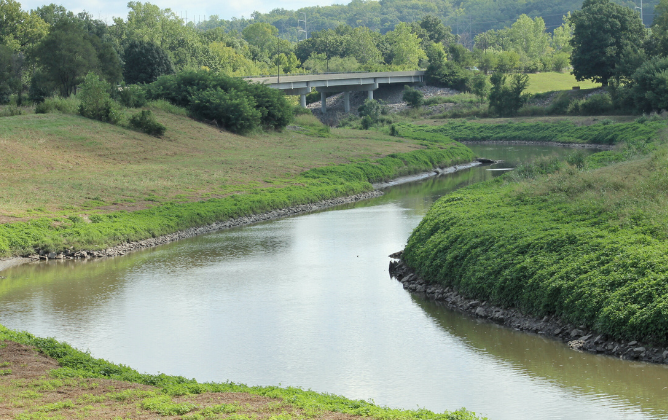Winding river along lush green terrain with freeway bridge in the background