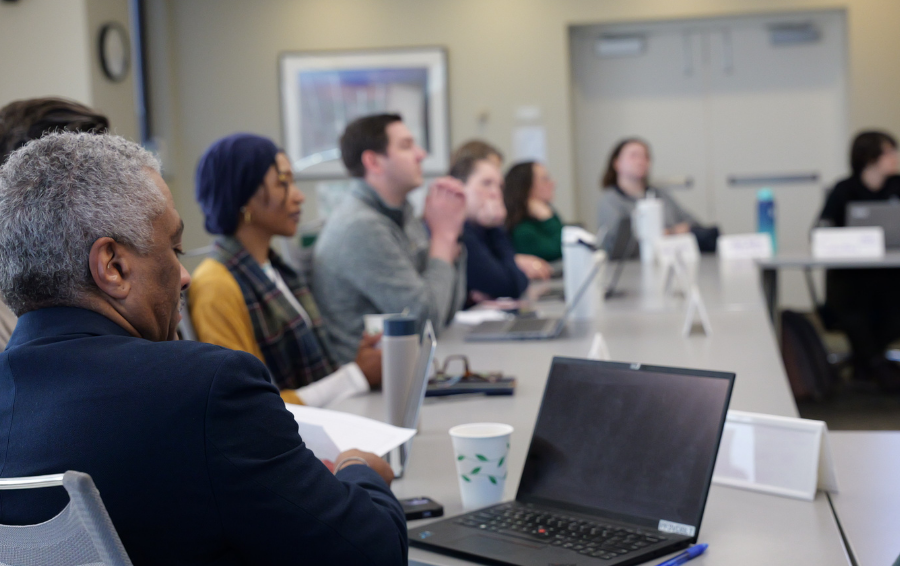 People gathered at a large roundtable with laptops and notebooks