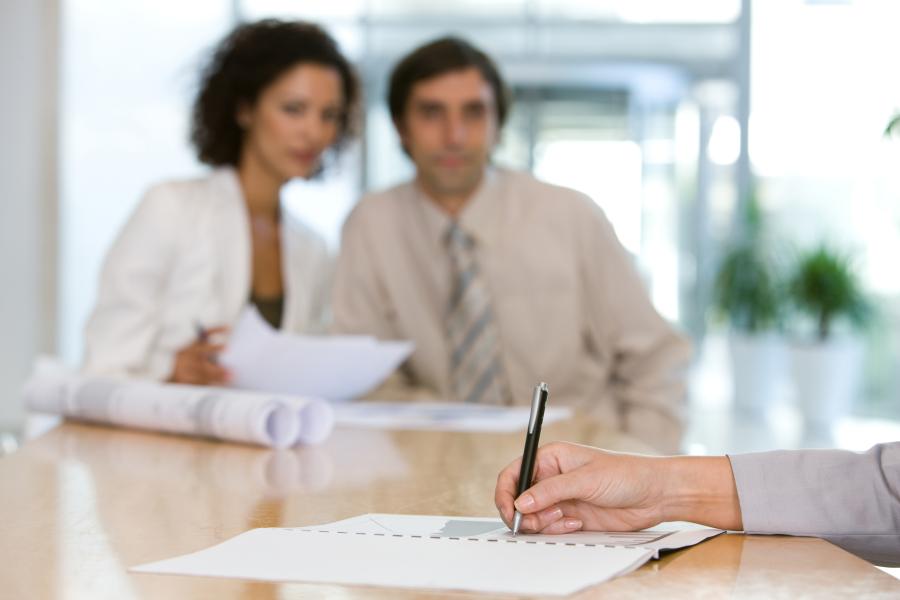 Person writing notes with a pen as two co-workers look at them 