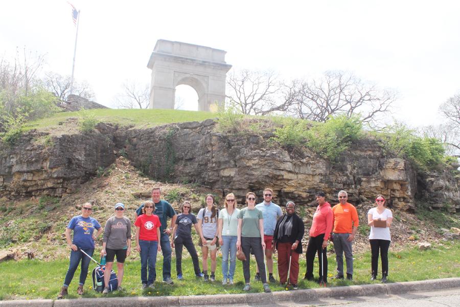 A group holding litter clean up tools below the Rosedale Arch in KCK