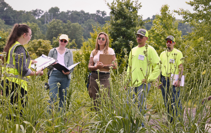 Training coordinator describes native plant installation to participants with clipboards and high-vis clothing