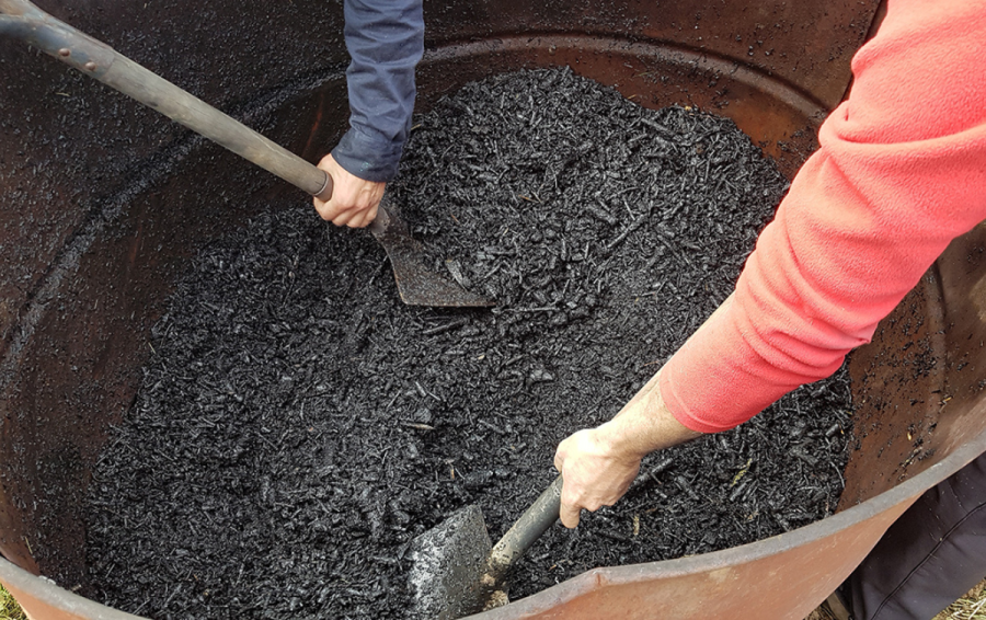 workers mix up black organic material in a bin with shovels