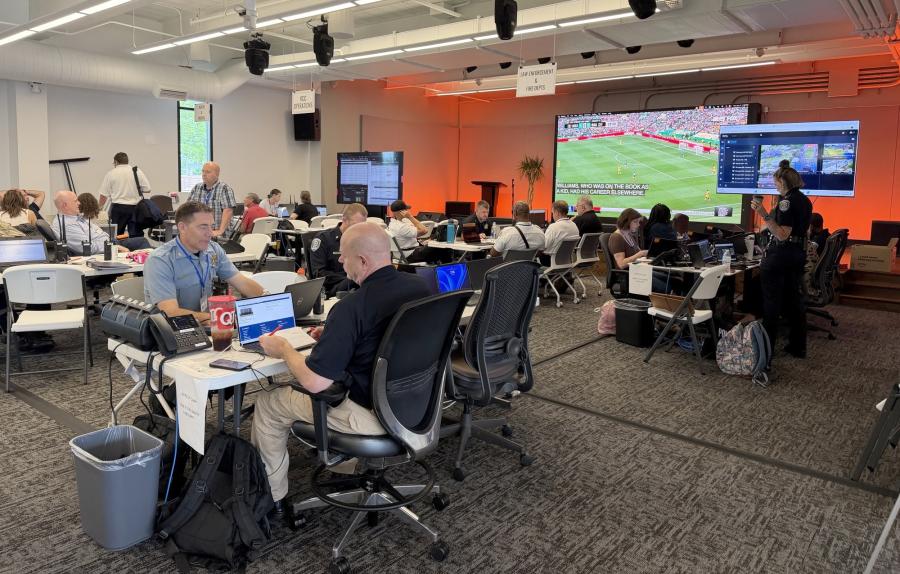 A room full of people sitting at tables with a soccer match on a screen