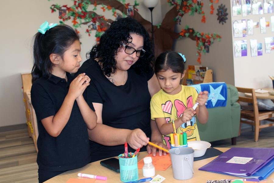 A woman with two young students at a table doing a craft