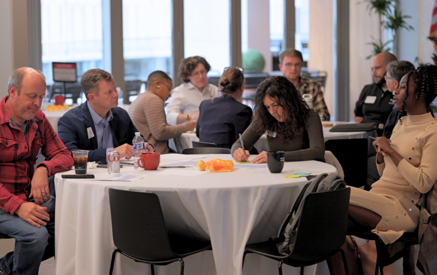 Attendees gathered around a table, talking and jotting down notes.